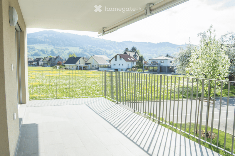 Balcony with metal railing, tiled floor, and scenic view of a valley and houses.