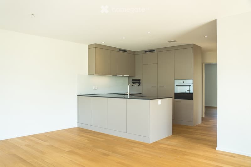 Modern kitchen with light grey cabinets, a central island, and a black countertop. Features include a stainless steel sink, a built-in oven, and recessed ceiling lighting.
