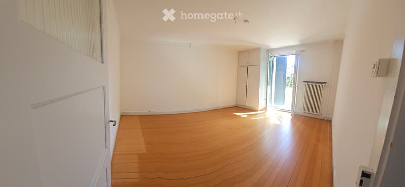 Empty room with wooden flooring, white walls, and a door leading to a balcony. A small cabinet and radiator are visible.