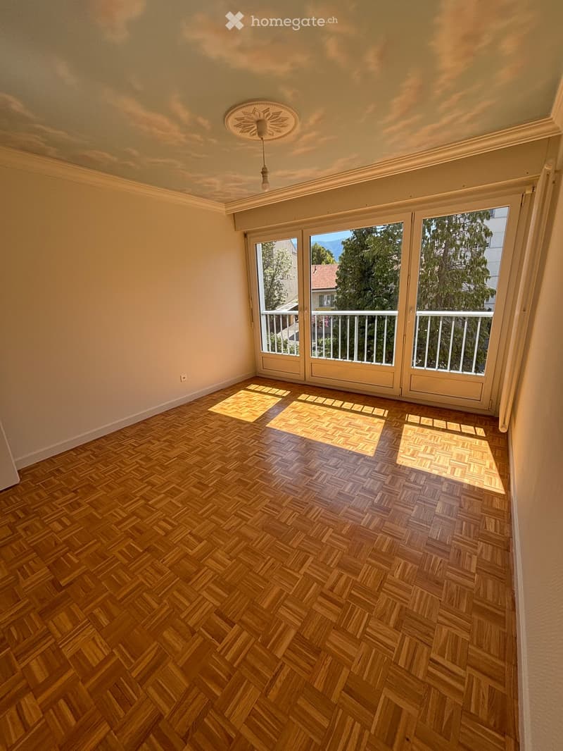 Empty room with wooden herringbone flooring, large sliding glass doors leading to a balcony, and a decorative ceiling light fixture.