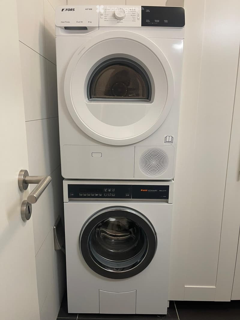 A compact bathroom with a stacked washing machine and dryer unit, featuring modern control panels and a sleek design.