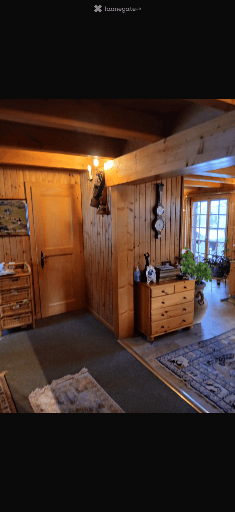 A cozy, wooden-paneled hallway with a drawer, picture frame, plant, clock, and a door leading to another room.