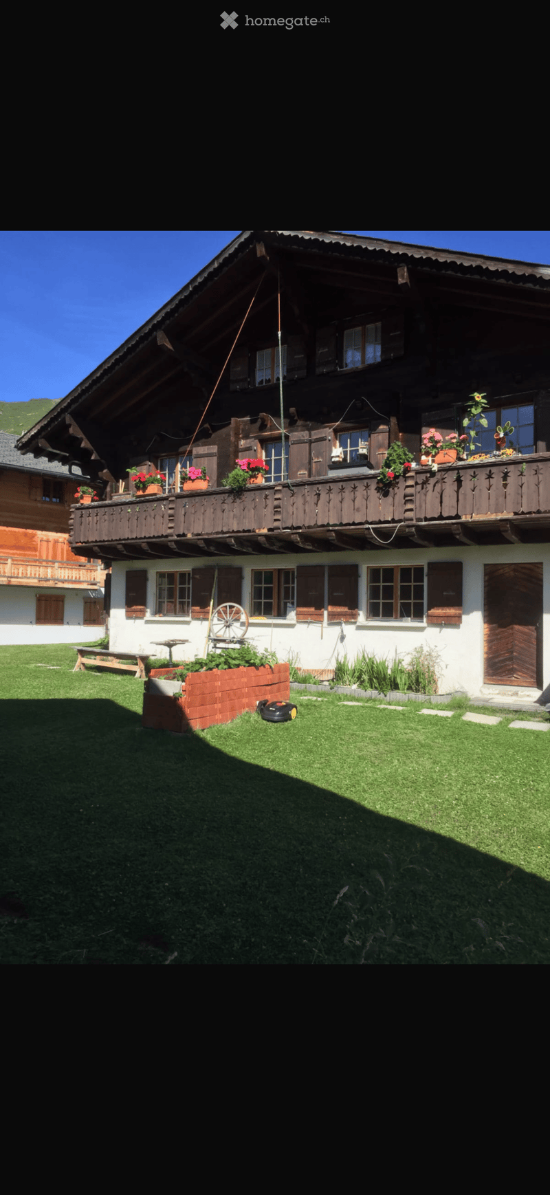 Traditional two-story wooden house with a large balcony, multiple windows, and a well-maintained lawn.