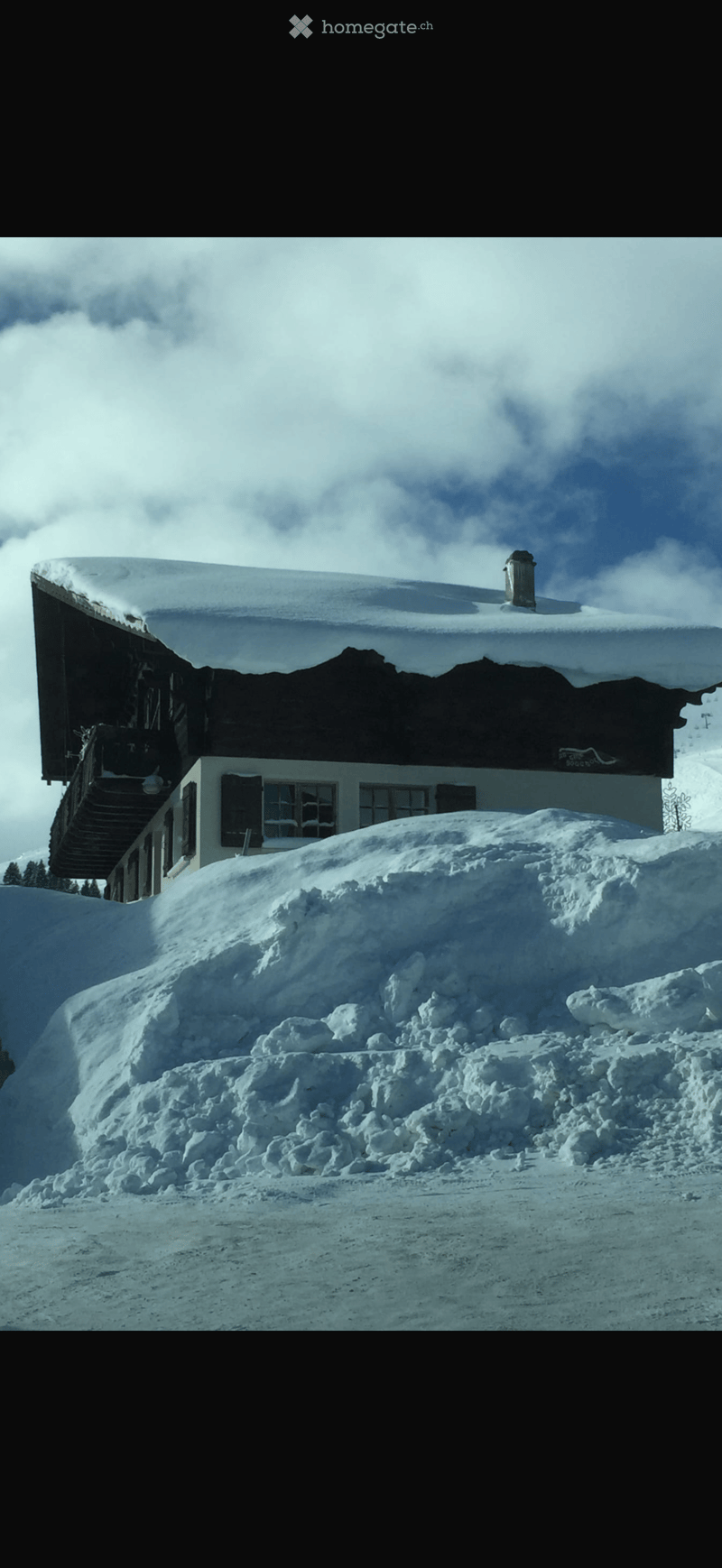 A two-story wooden building with snow-covered roof and windows, surrounded by a large pile of snow.
