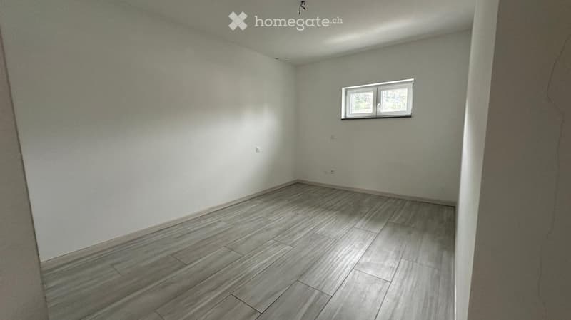 Empty room with light grey walls and a grey wooden floor, featuring a single window with white frame and glass panels.