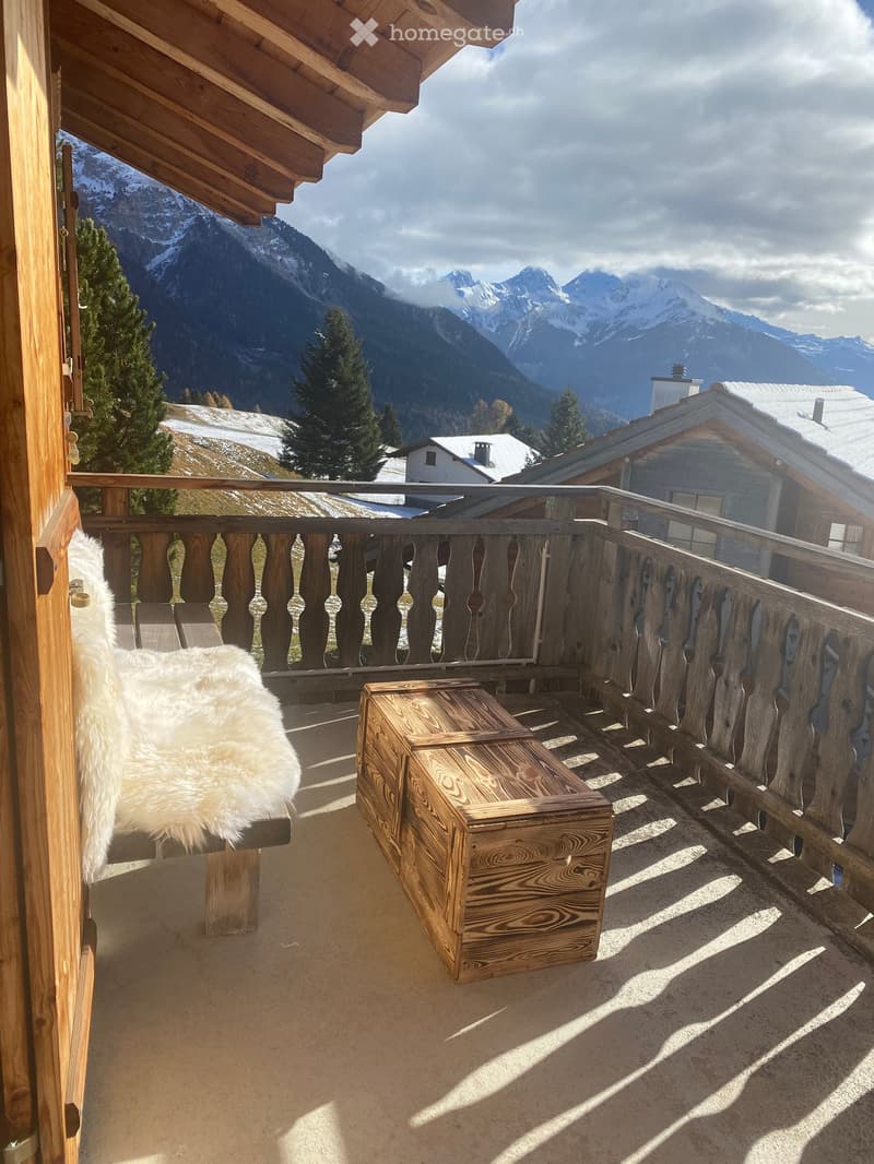 Balcony with wooden railing, bench with fur throw, wooden chest, overlooking snow-capped mountains.