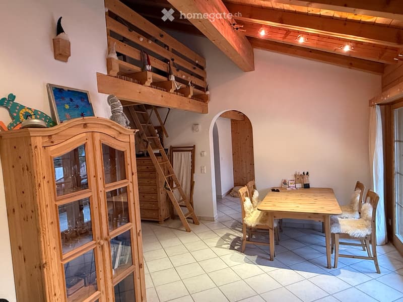 A cozy, wooden-furnished room with a dining table, chairs, a wooden cabinet, and a small loft area with a ladder.