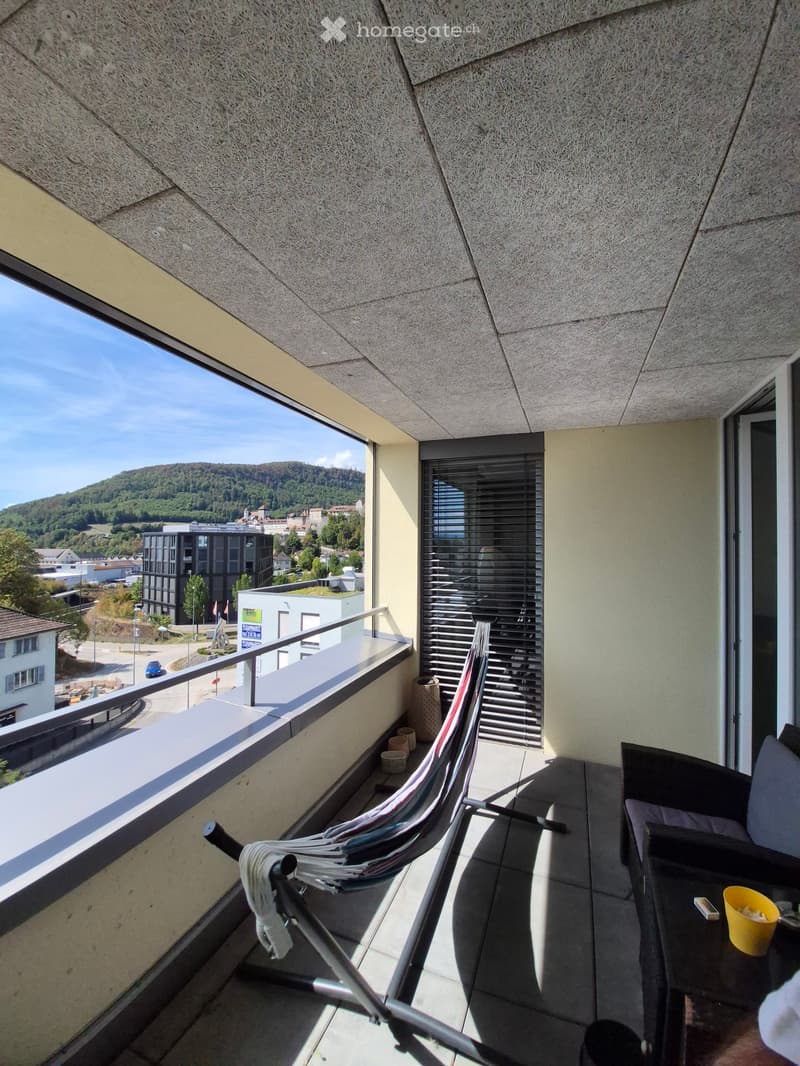 Balcony with modern furniture, overlooking a cityscape and hills.