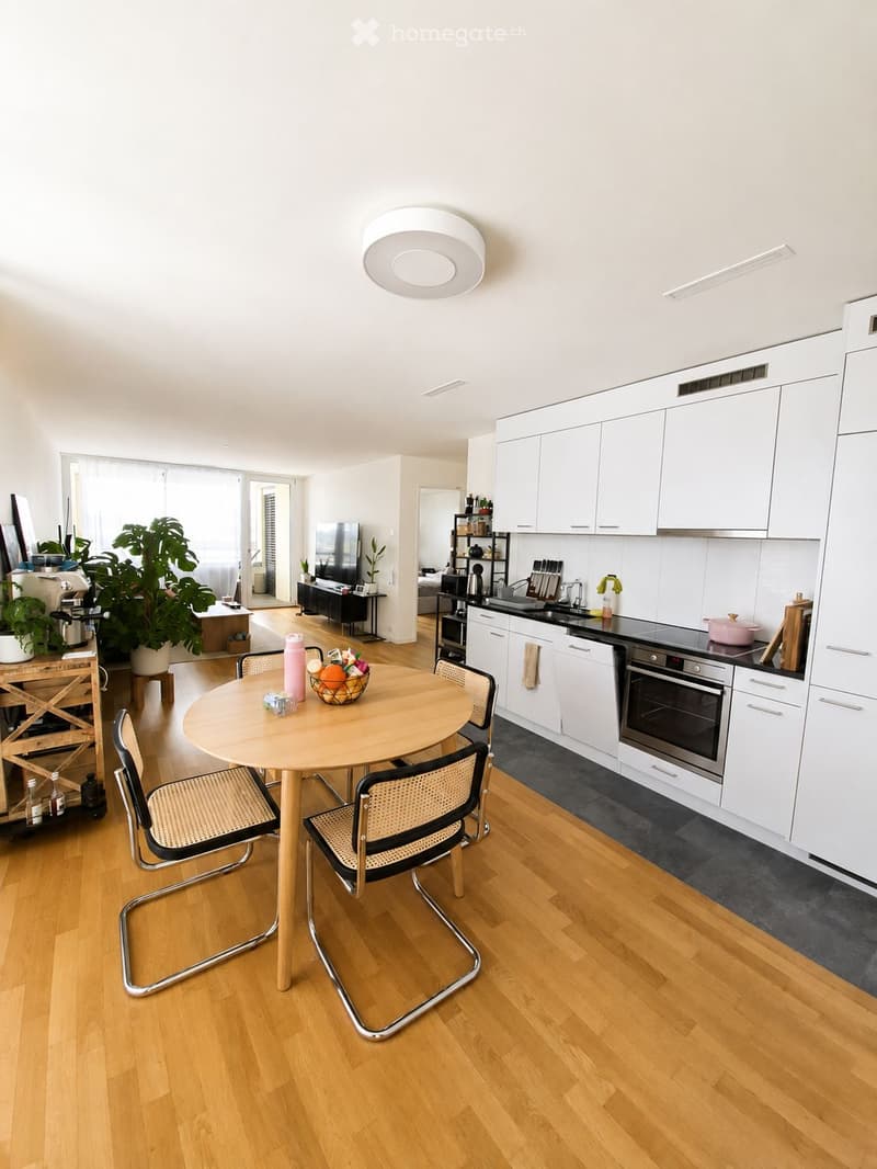 Modern kitchen with white cabinets, wooden floor, round dining table with four chairs, and various appliances including an oven and sink.