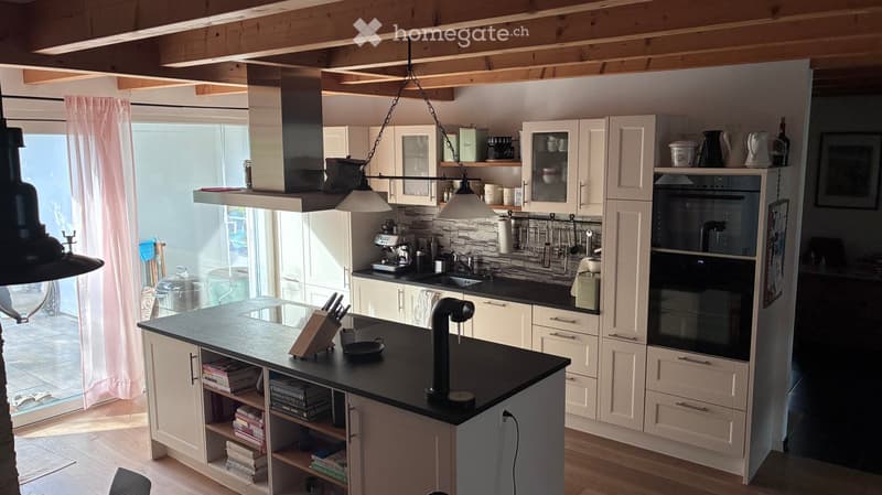 Bright, modern kitchen with white cabinets, black countertops, and a central island. Features include a built-in oven, pendant lights, and various kitchen utensils and appliances.