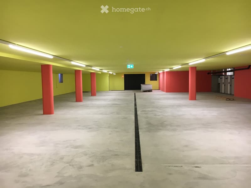 Empty underground parking area with concrete floors, yellow and red painted walls, red support pillars, and fluorescent lighting.