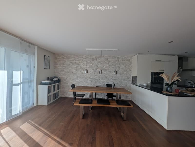 Modern kitchen and dining area with wooden flooring, white cabinets, a stone accent wall, and a wooden dining table with chairs.