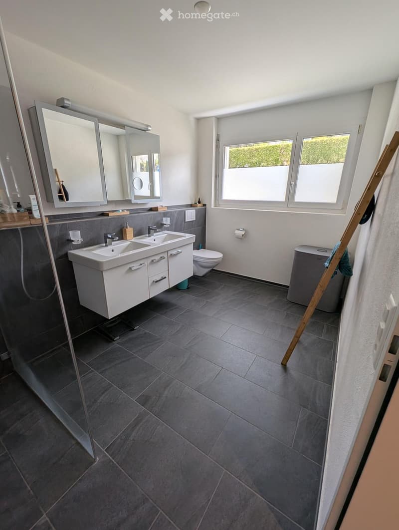 Modern bathroom with double sink, large mirror, toilet, and grey tiled floor.