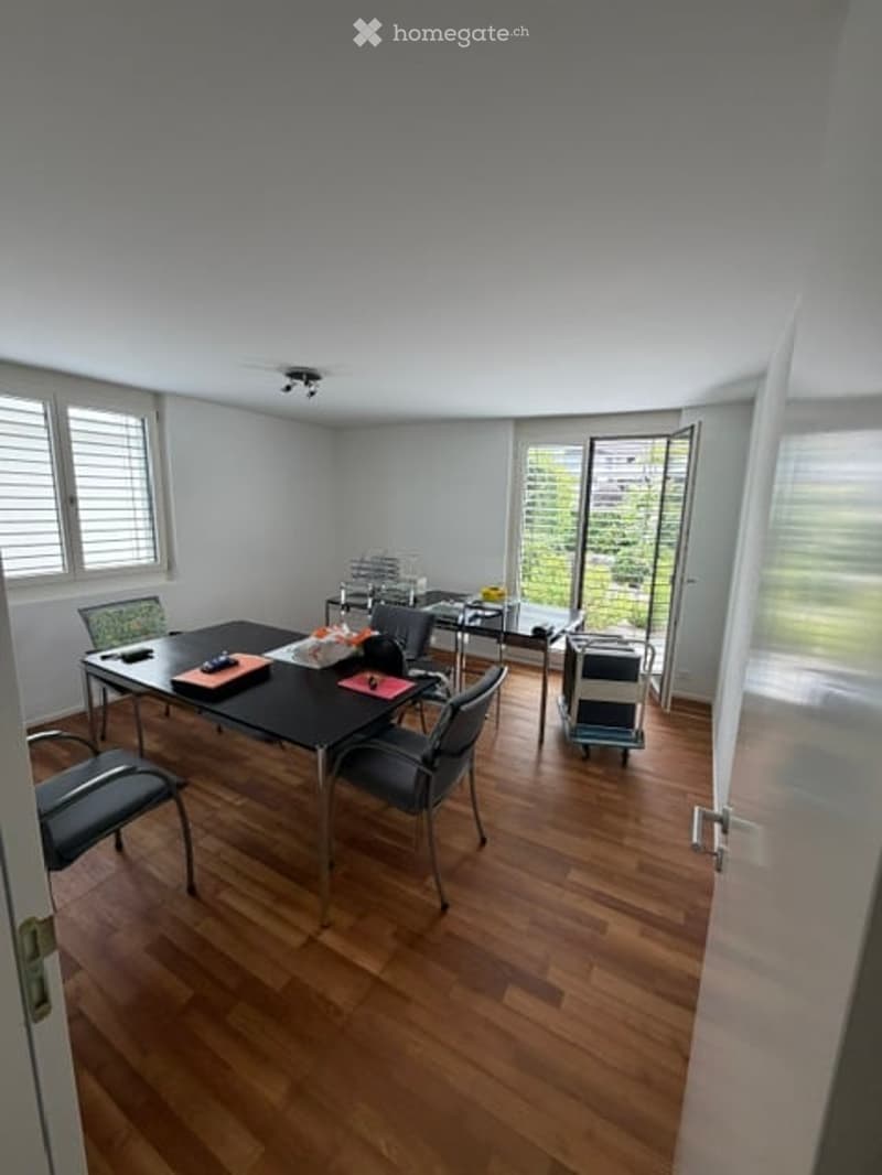 Dining room with wooden floor, large windows, and a table with chairs and a laptop.