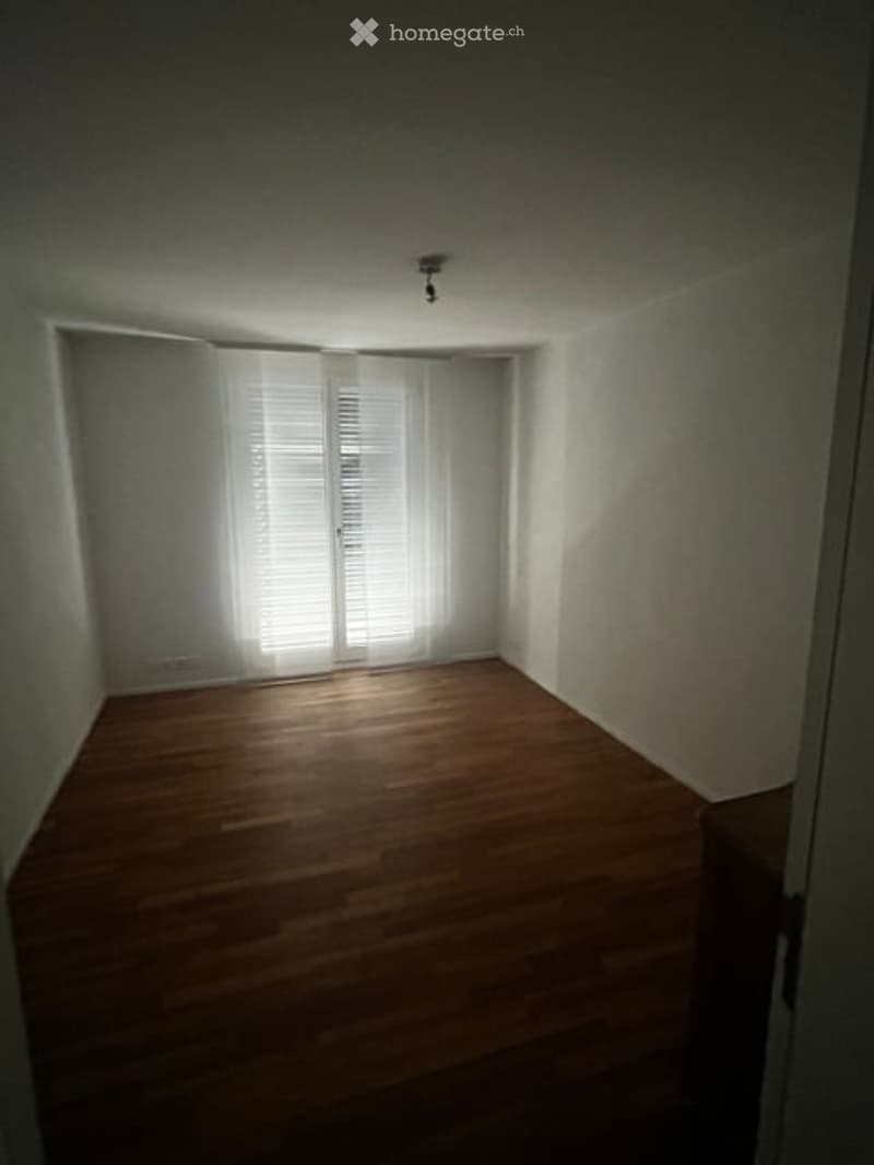 Empty room with wooden flooring, white walls, and a set of double doors with blinds.