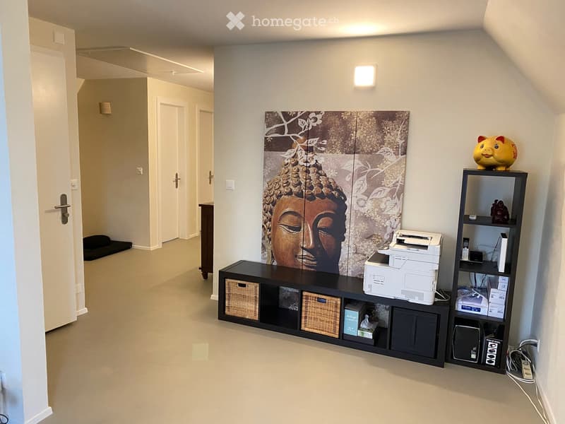 A furnished room with a large Buddha head picture on the wall, a black cabinet with wicker baskets, a printer, and a shelf with various items including a piggy bank.