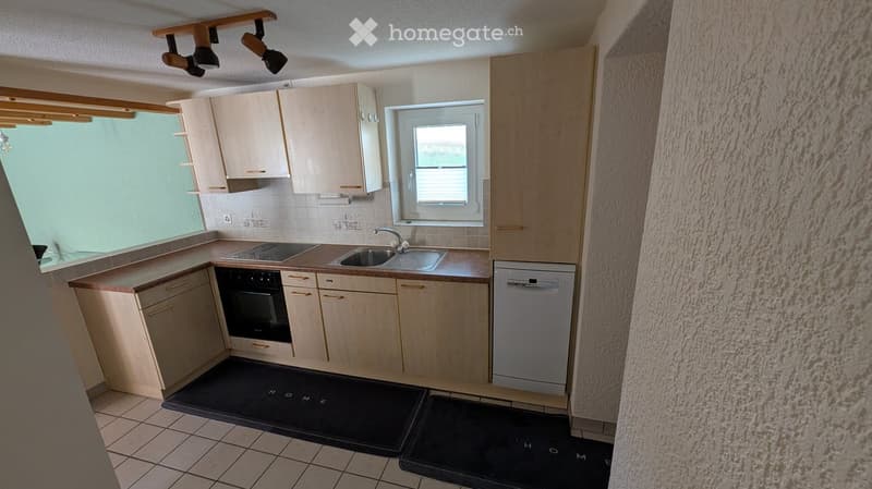 Modern kitchen with light wood cabinets, stainless steel sink, oven, and dishwasher. Features a large window and track lighting.