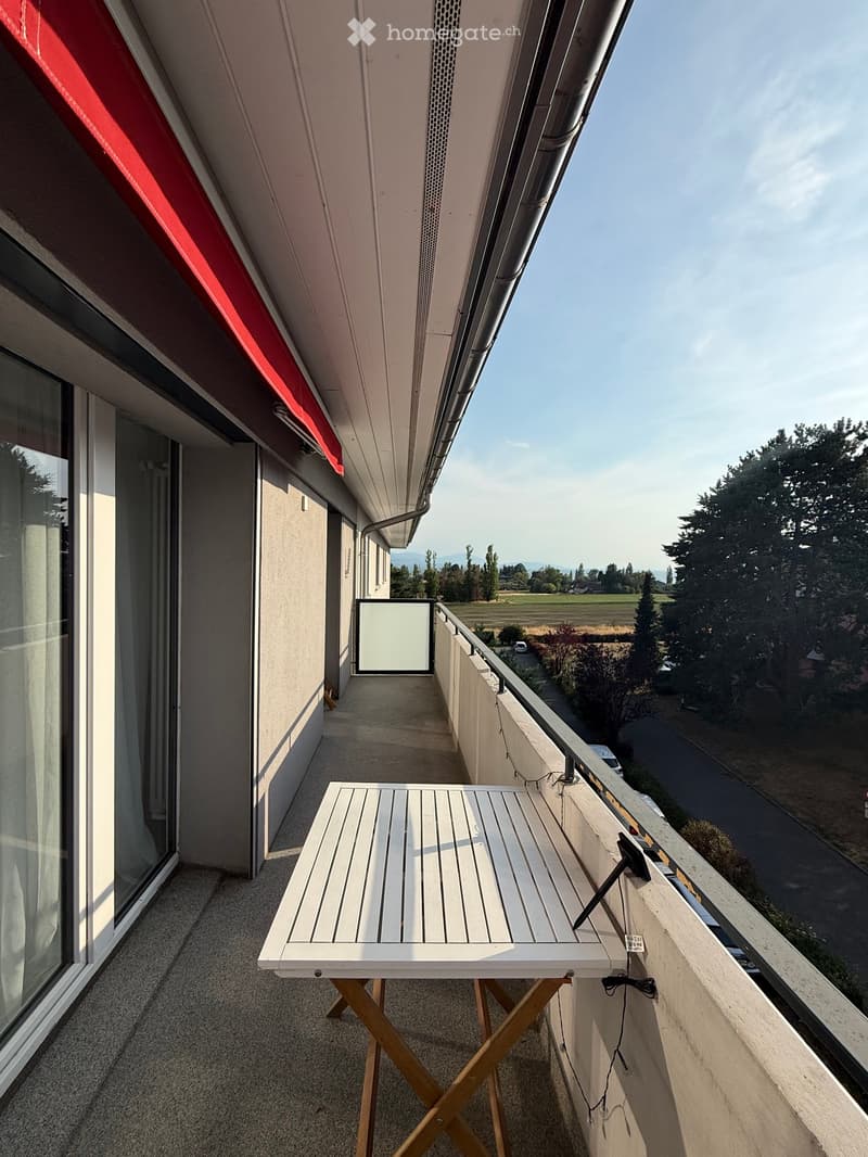 Balcony with a small white table, overlooking a rural landscape with fields and trees.