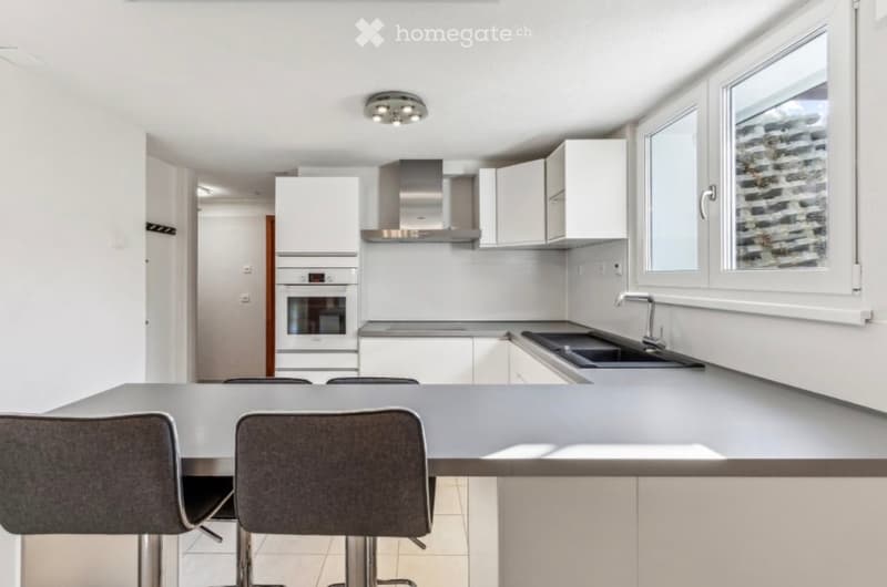 Modern kitchen with white cabinets, stainless steel appliances, a central island with bar stools, and large windows.