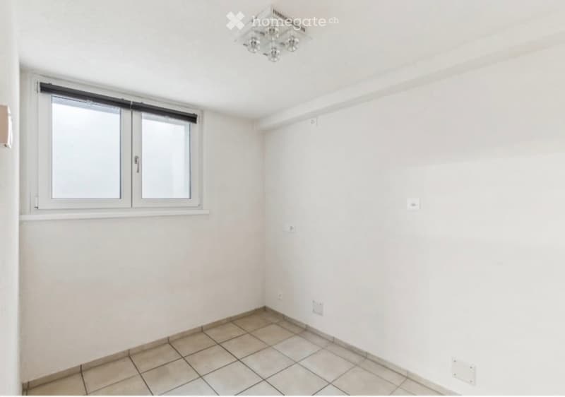 Empty room with white walls, tiled floor, and a window with blinds. No furniture or equipment present.