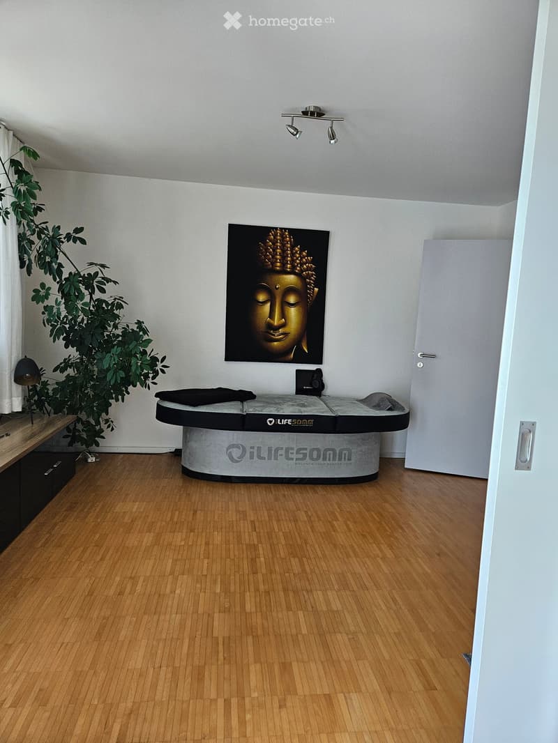 A modern, minimalist room with a massage table, a large Buddha picture, a plant, and a lamp.