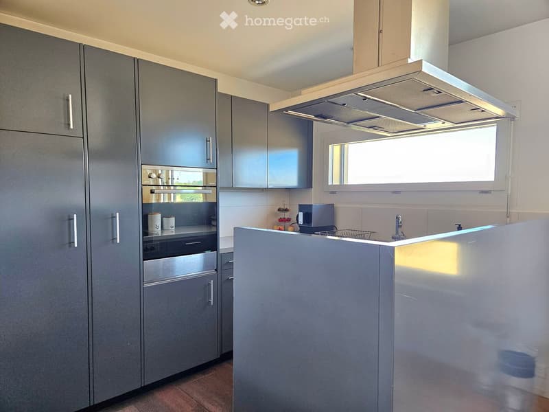 Modern kitchen with grey cabinets, stainless steel oven, and a central island with a sink and faucet.