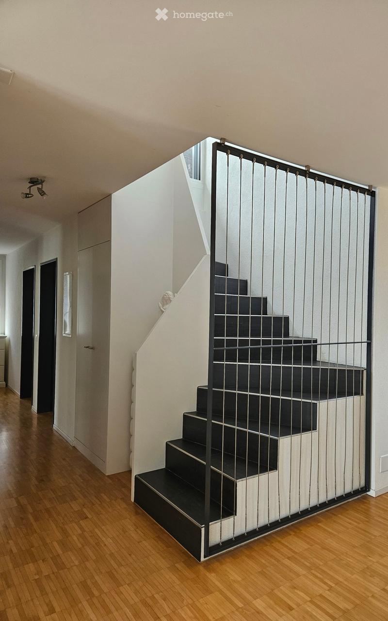 Modern hallway with wooden flooring, black staircase with metal railing, white walls, and recessed lighting.