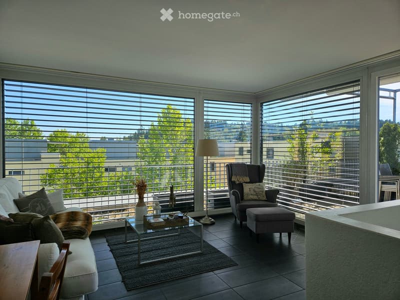 Modern living room with large windows, balcony access, sofa, armchair, coffee table, floor lamp, and decorative items.