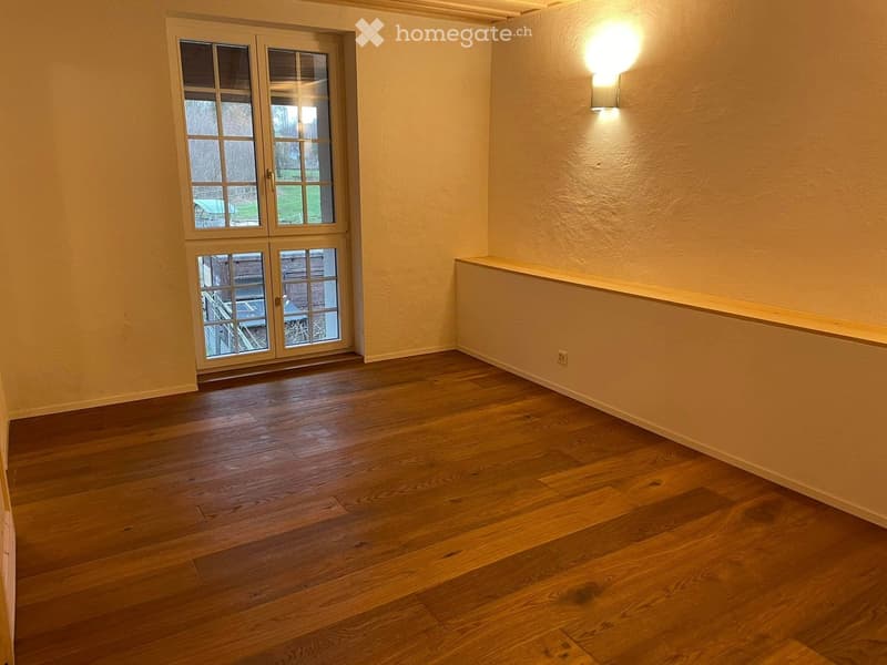Empty room with wooden flooring, large windows, and a wall-mounted light fixture.