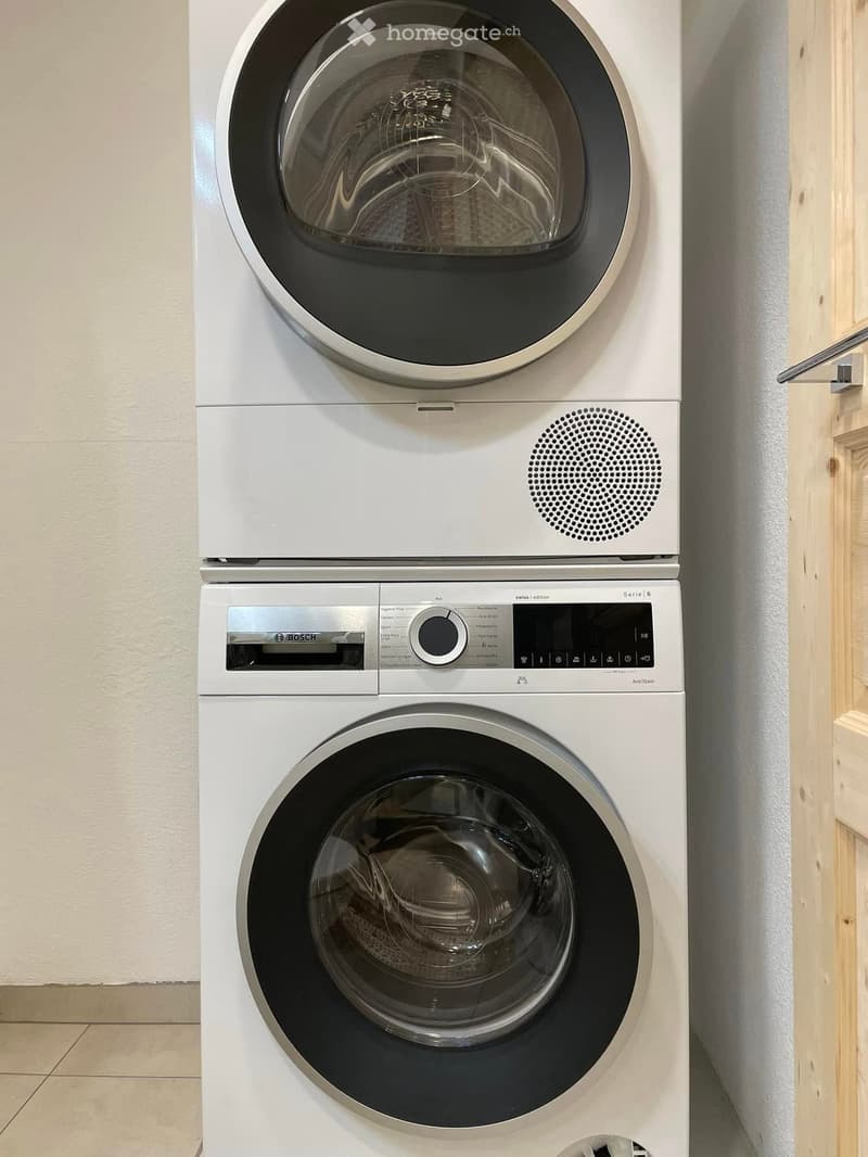 A modern Bosch washing machine and dryer combo unit is installed in a bathroom, featuring sleek white design and digital control panels.