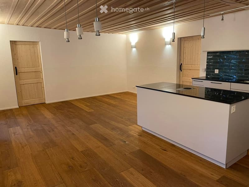 Modern kitchen with light wooden flooring, white cabinets, black countertop, and pendant lights.