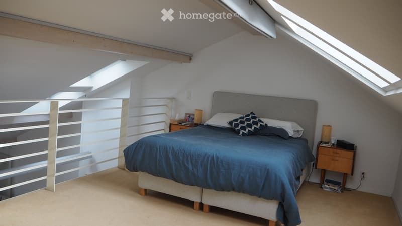 Cozy attic bedroom with skylights, a grey upholstered bed, nightstands, and decorative pillows.