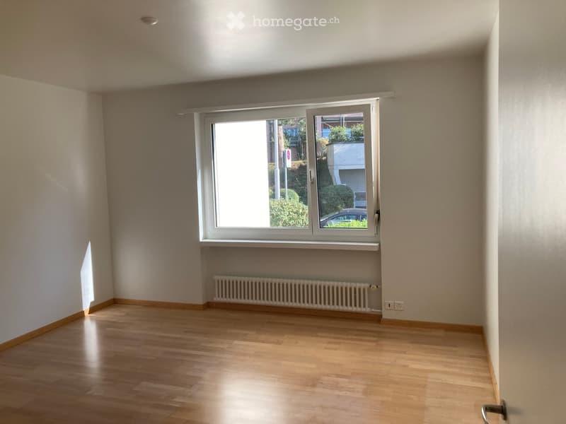 Empty room with wooden flooring, white walls, a large window with blinds, and a radiator below the window.