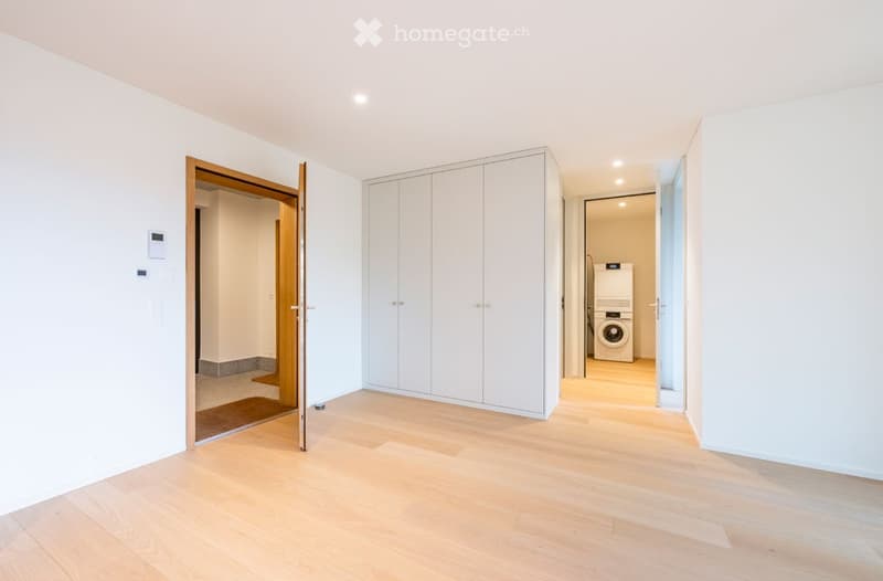 Empty room with light wooden flooring, white walls, built-in white closet, and an open doorway leading to a laundry area with a washing machine.