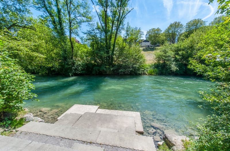 A serene outdoor area featuring a clear river flowing through a lush, green landscape with trees and vegetation on both banks.