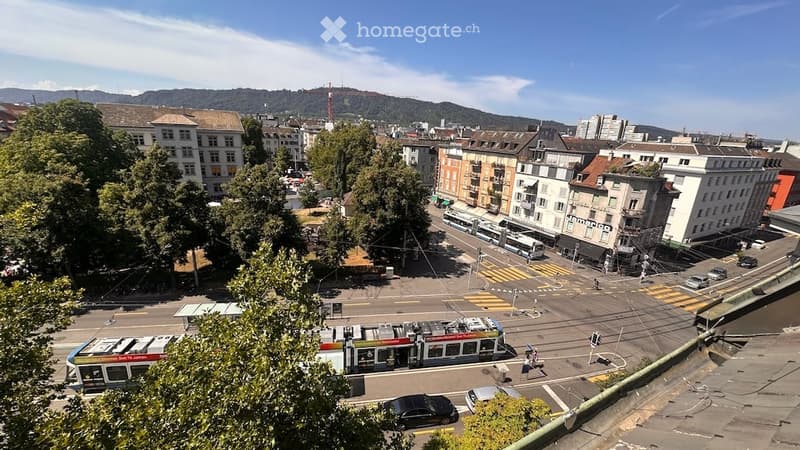 A panoramic view of a city street with buildings, trams, and a distant mountain range.