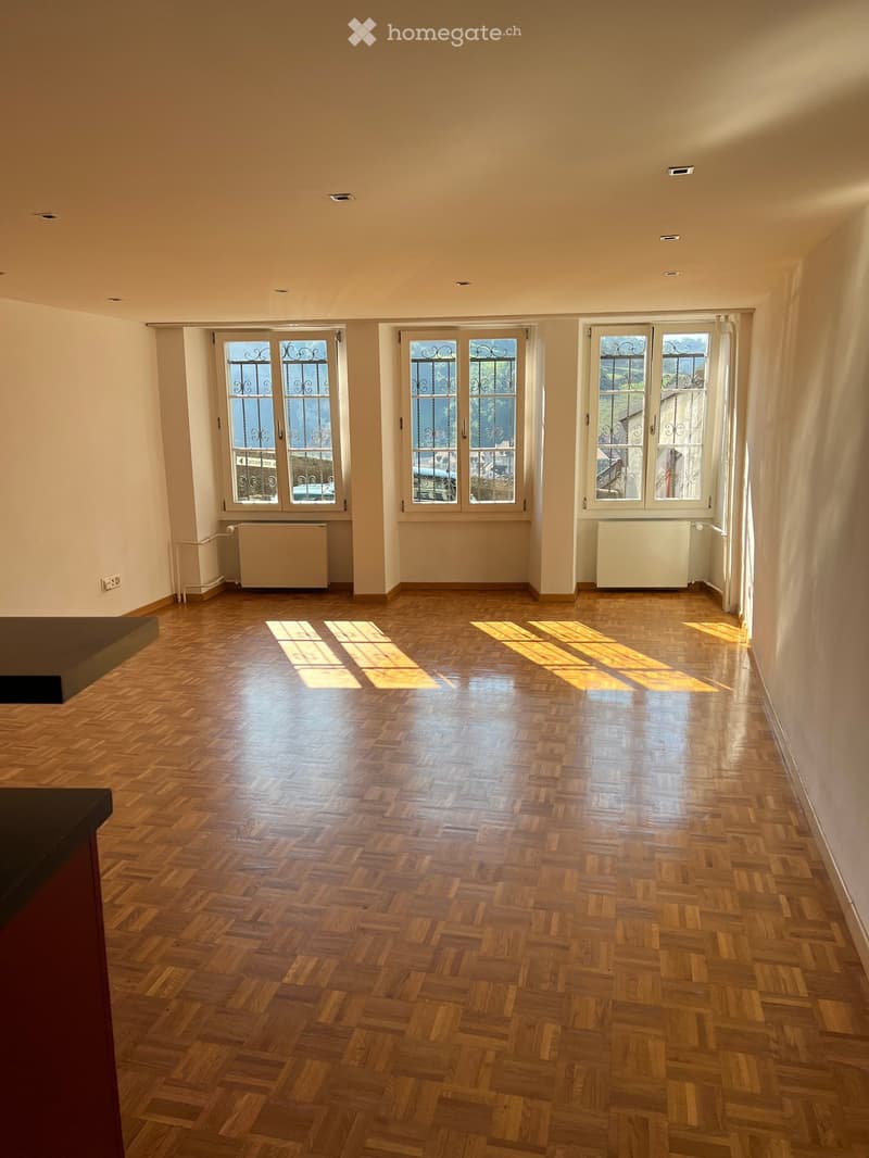 Empty room with wooden herringbone flooring, large windows with decorative metal grilles, radiators, and recessed ceiling lighting.