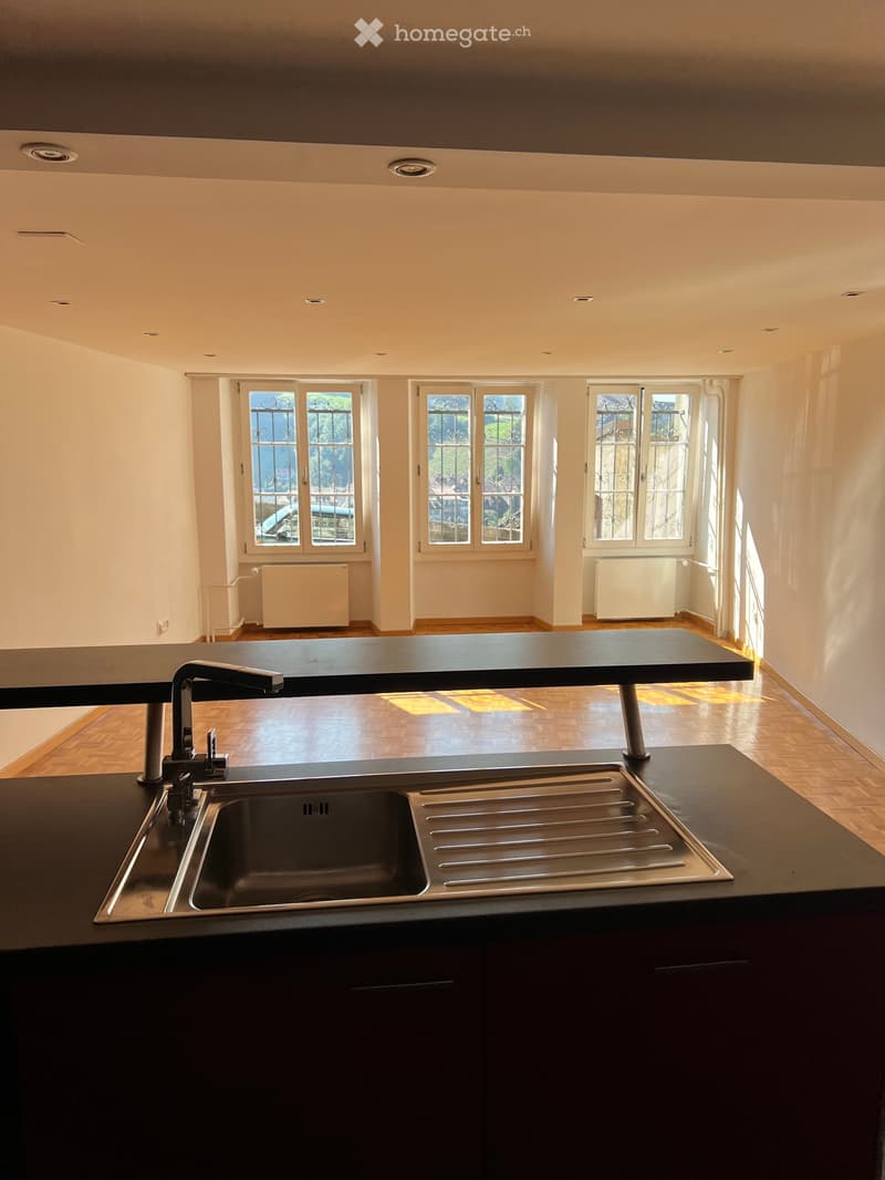 Modern kitchen with dark countertops, stainless steel sink, and large windows with decorative grilles. The space features wooden flooring and built-in cabinets.