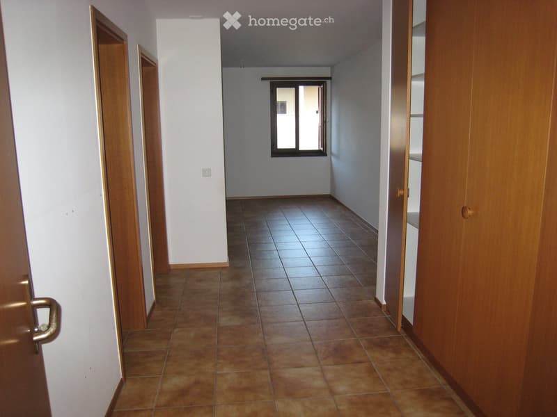 Empty hallway with tiled floor, white walls, and wooden doors on both sides. A window is visible at the far end.