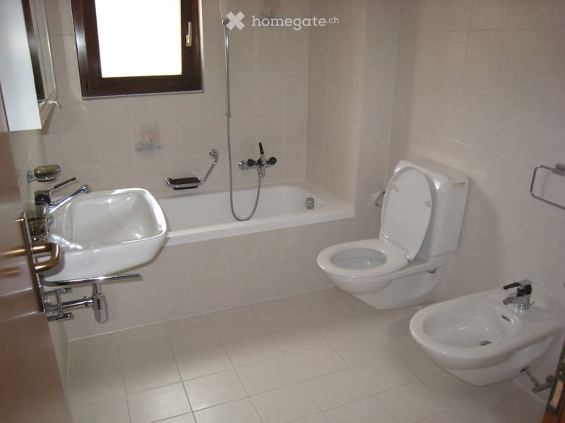 Modern bathroom with a white sink, bathtub, toilet, and bidet, all featuring silver fixtures and a large window for natural light.