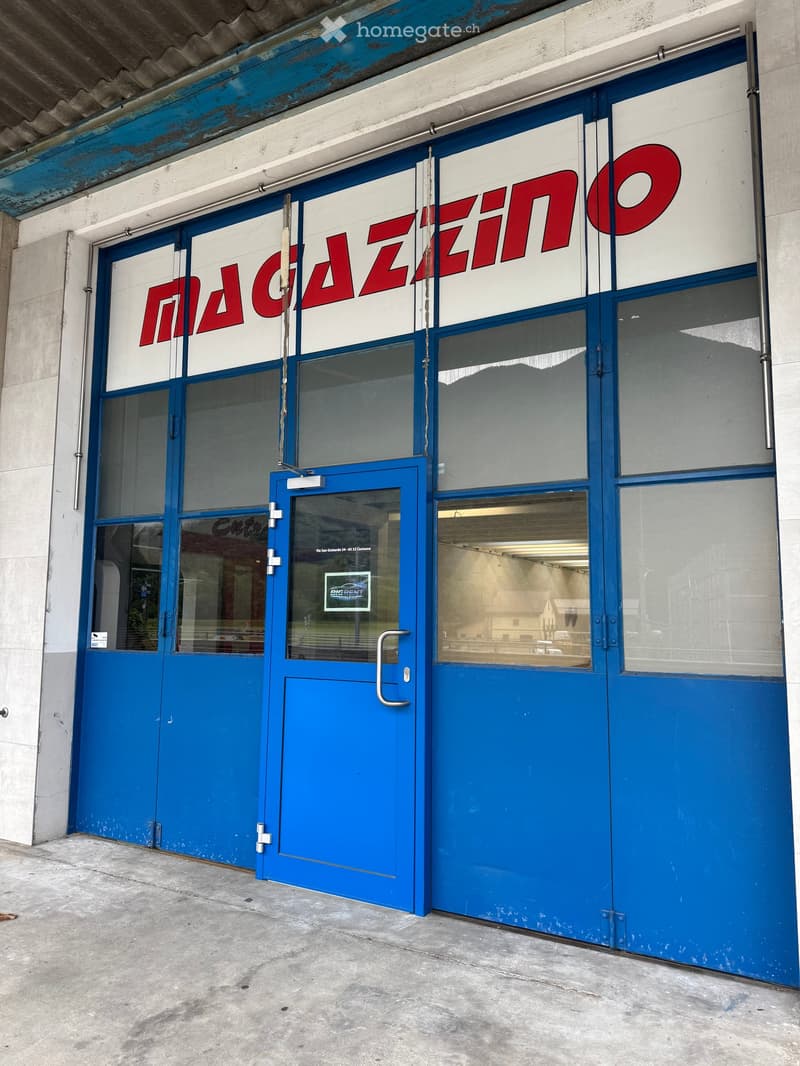 Exterior view of a commercial building with blue doors and large windows, featuring a sign that reads "MAGAZINO" in red letters.