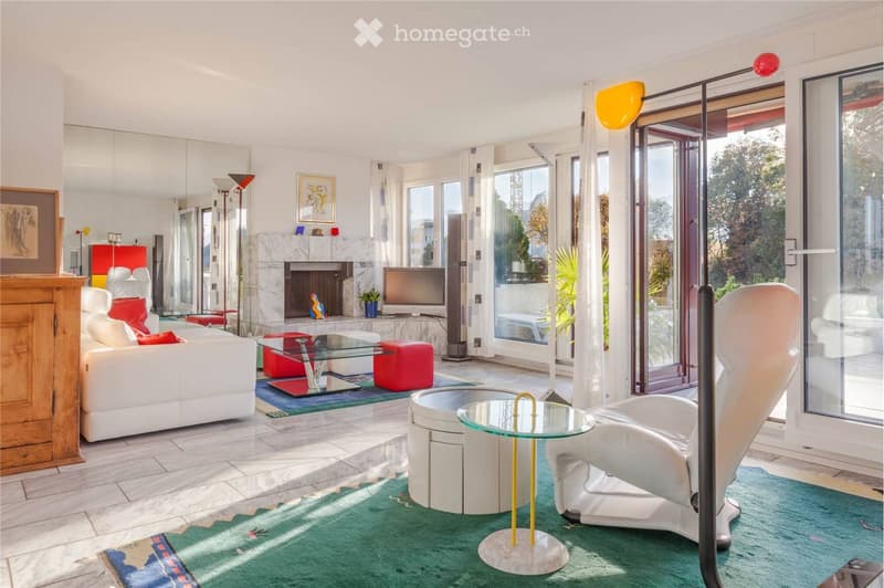 Modern living room with white leather sofa, white armchair, glass coffee table, fireplace, TV, and large windows offering a view.