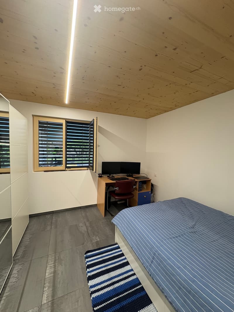 Modern, minimalist bedroom with a single bed, desk with computer, chair, and a small rug.