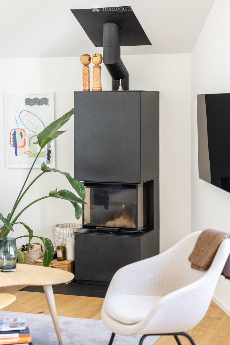 Modern living room with a sleek black fireplace, white chair, wooden coffee table, and decorative plant.