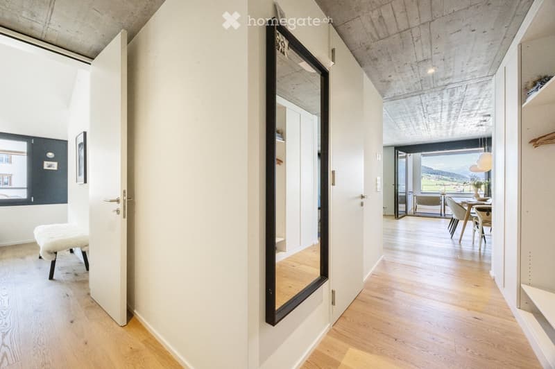 Modern hallway with wooden flooring, white walls, large mirror, and open doors leading to adjacent rooms.