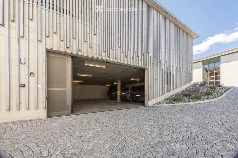 Modern building with a large garage entrance, several parked cars inside, and a sleek, contemporary design featuring vertical wooden slats on the facade.