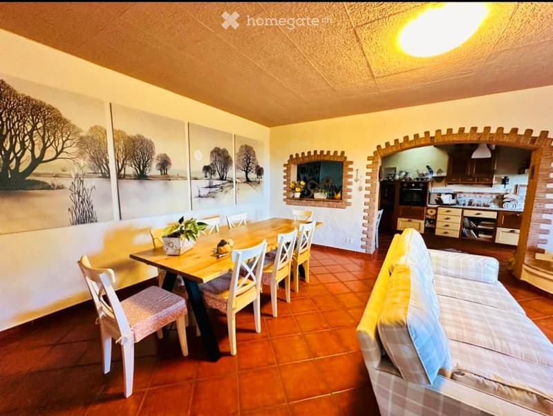 A cozy living and dining area with a sofa, dining table, chairs, and a small kitchen area visible in the background.