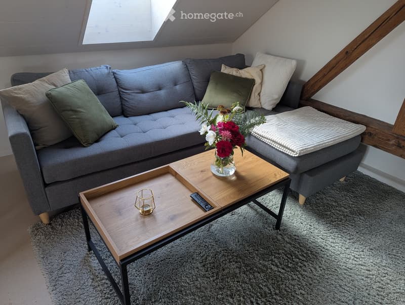 Cozy living room with grey sectional sofa, wooden coffee table, decorative vase with flowers, and a small candle holder.