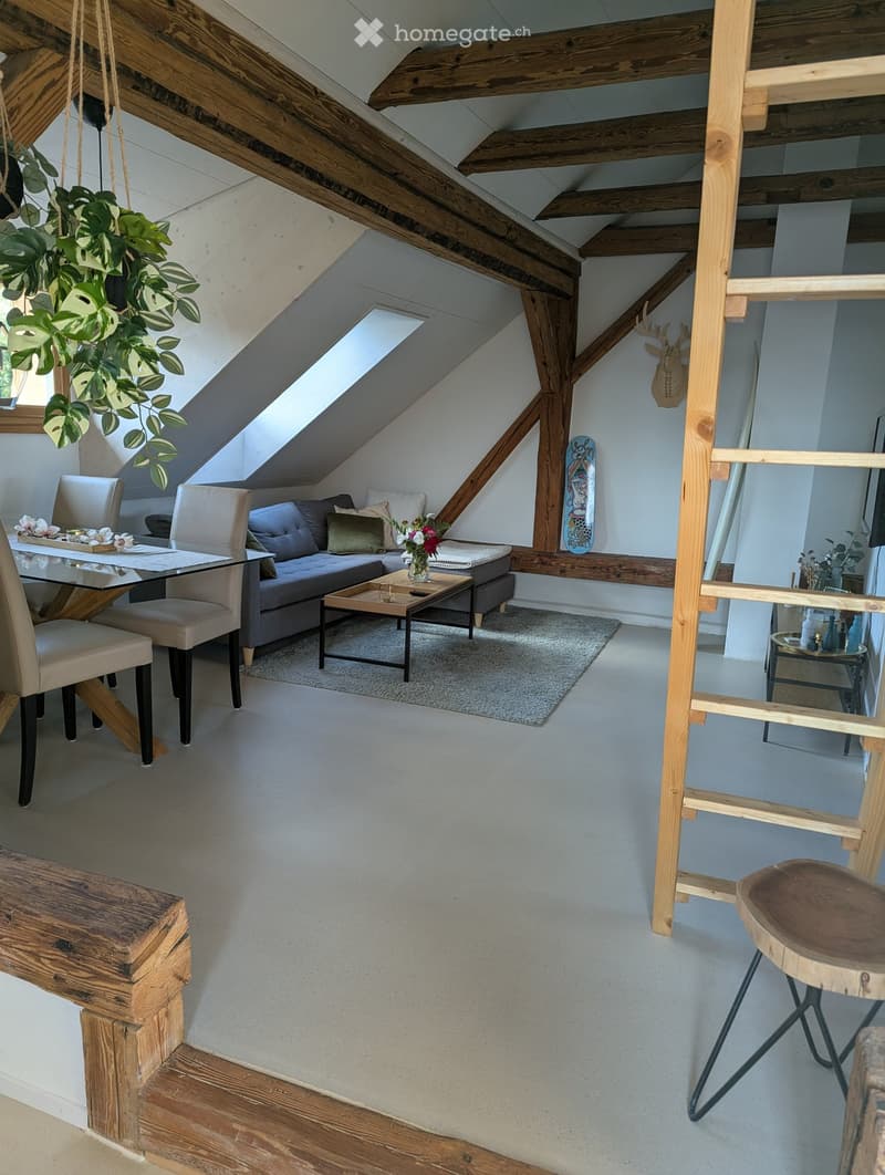 Loft-style living room with exposed wooden beams, skylight, grey sofa, coffee table, dining table, and chairs.
