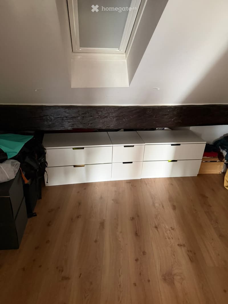 Empty room with light wooden flooring, white built-in storage units, and a dark wooden trim along the wall.